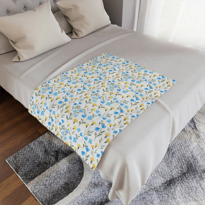 blue and yellow wildflower print on a plush throw blanket, blue and yellow floral throw blanket lying on a bed